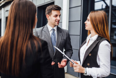 three-cheerful-young-business-people-talking-each-other-while-walking-outdoors (1)